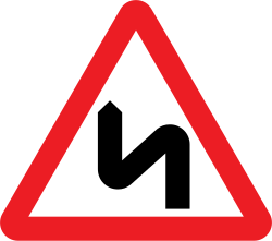 UK double bend warning sign: a red-bordered triangle with a black S-shaped arrow, first bend to the left